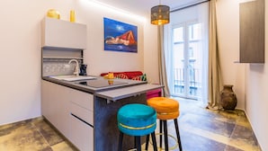 A modern kitchen with a central island, bar stools, a painting, and a view to the outside. - Golden Shell at Hystorical Center (Naples)