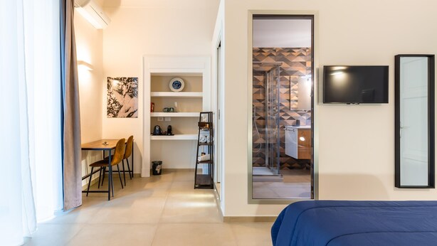 A modern hotel room with a bed, a desk with chairs, a TV, and a bathroom visible through an open door. - Caracciolo in Naples (Naples)