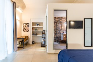 A modern hotel room with a bed, a desk with chairs, a TV, and a bathroom visible through an open door. - Caracciolo in Naples (Naples)