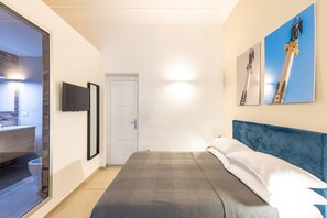 Quarto com cama, cabeceira azul e duas pinturas penduradas na parede.
