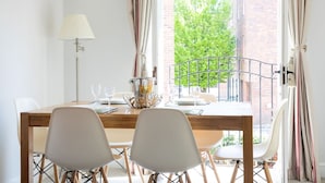 A dining table set for four with a metal railing outside, a lamp, and a view of a brick building and greenery.