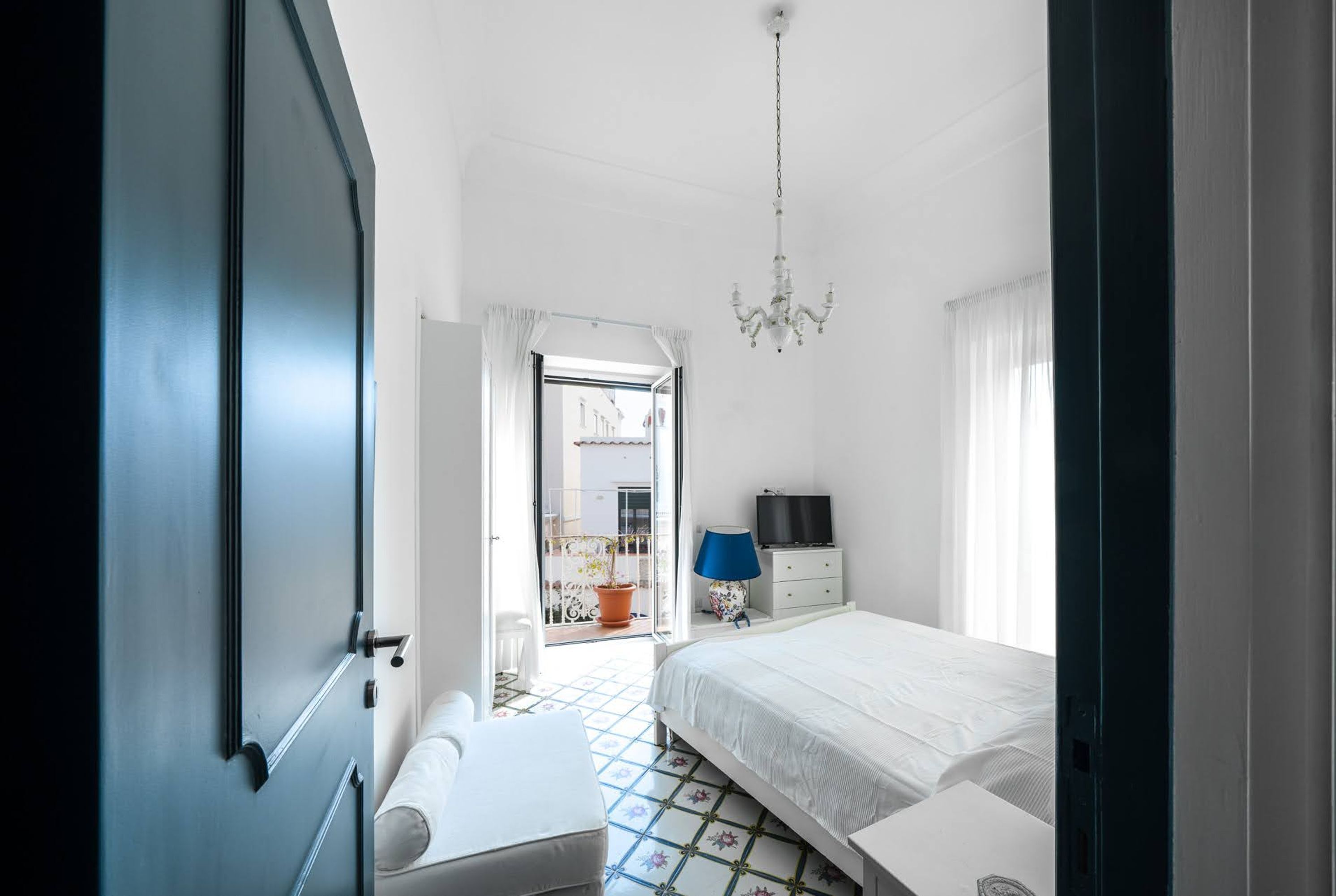 A bedroom with a bed, a desk, a chair, a TV, and a window.