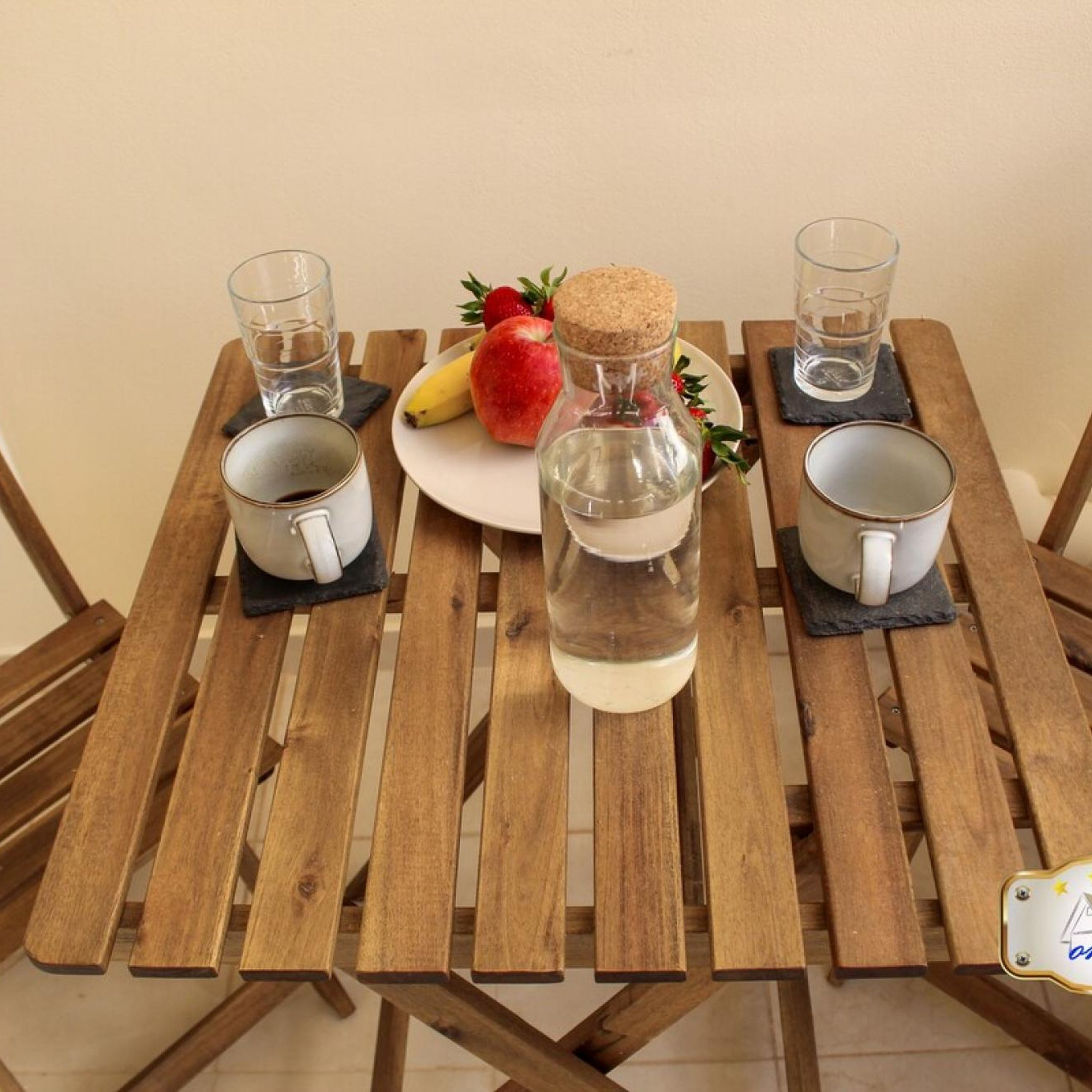 Une table en bois avec quatre tasses, une bouteille d’eau et une assiette de fruits.