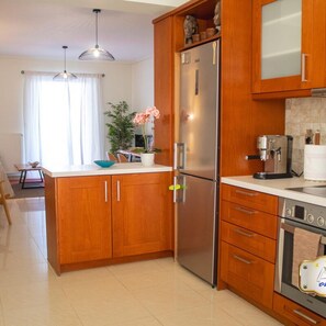 A modern kitchen with wooden cabinets, a stainless steel refrigerator, a coffee maker, and a tiled backsplash. - Filoxenia in the Centre of Kalamata (Kalamata)