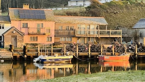 A canal with two boats docked, a building with a balcony, and a house in the background. - Littlefields in Seaton (Seaton)
