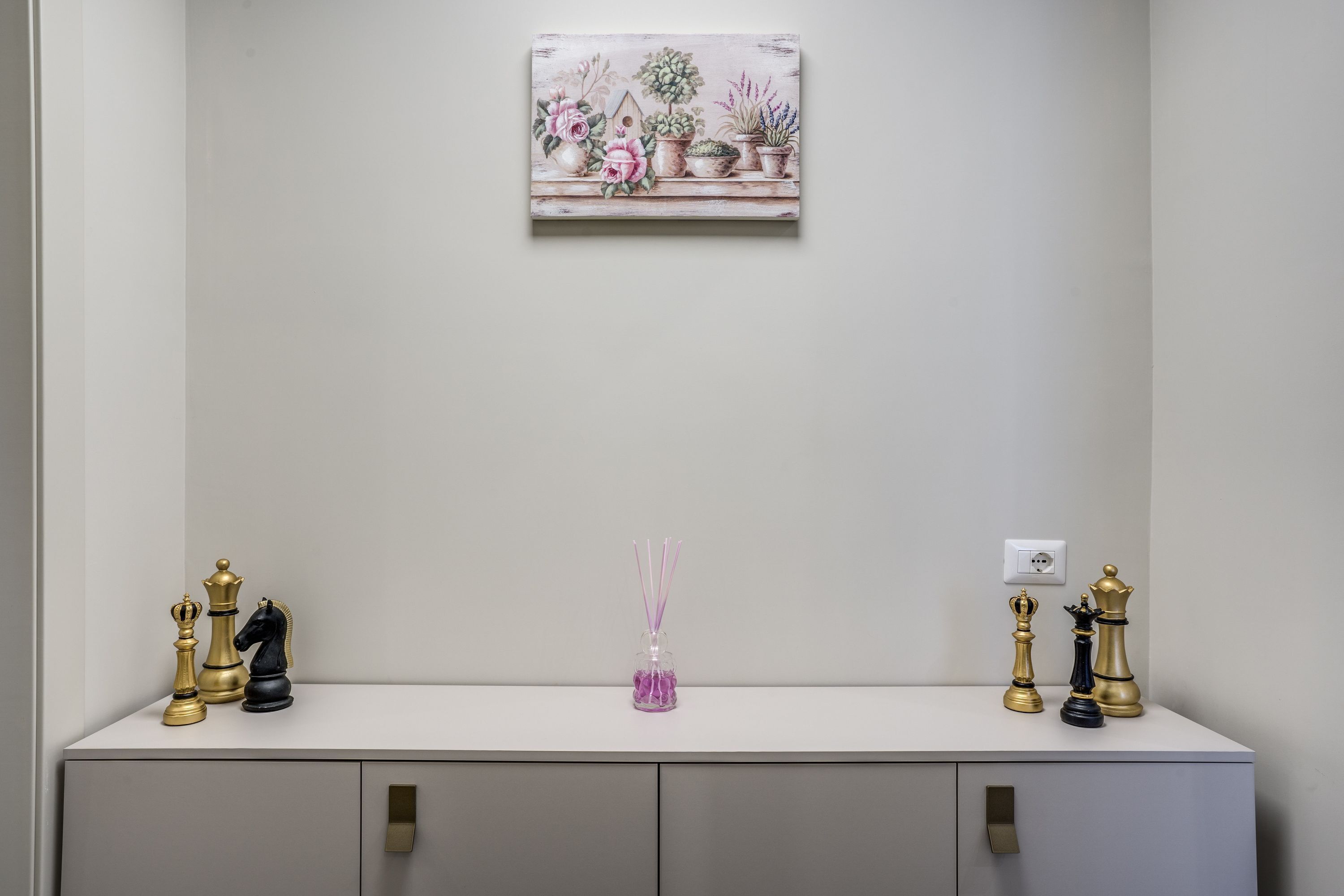 A white console table with chess pieces and a vase of purple flowers.