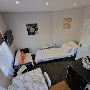 A hotel room with two beds, a desk, a chair, a TV, and artwork on the walls. - Stay Norwich Apartments Riverside House Apart-4 (Norwich)