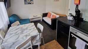 A compact hotel room with a dining table, a sofa, a small kitchenette, and a TV mounted on the wall. - Stay Norwich Apartments Riverside House Apart-4 (Norwich)