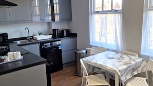 A compact kitchen with modern appliances, a dining area with a marble table, and a window with curtains. - Stay Norwich Apartments Riverside House Apart-4 (Norwich)