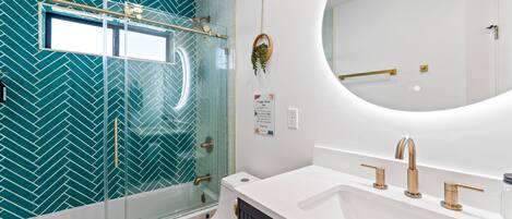 A modern bathroom with a glass shower enclosure, a white toilet, a vanity with a sink, and a large mirror.