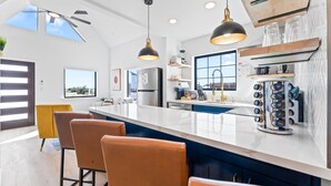 Une cuisine moderne dotée d’un grand îlot central, de luminaires suspendus et offrant une vue sur l’extérieur.