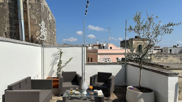 Terraza en la azotea con mobiliario de mimbre, una mesa con bebidas y aperitivos, y una planta en maceta.