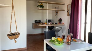 Un comedor con una mesa dispuesta para dos personas, una cesta colgante, un microondas, un tostador y una planta en maceta sobre una estantería.