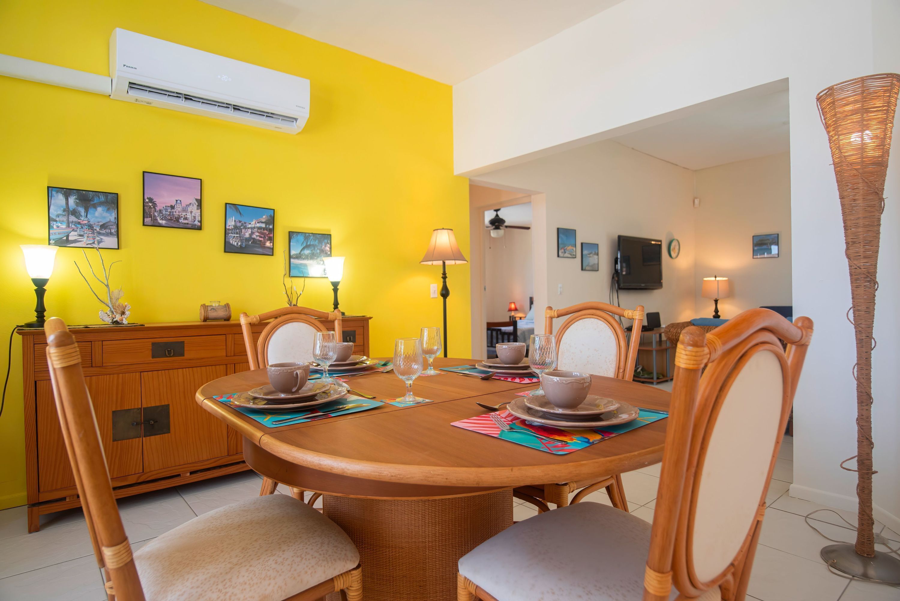 A dining area with a yellow wall, wooden furniture, and a TV in the background.