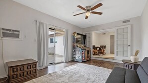 Un salón espacioso con un tapete grande, un ventilador de techo y un cristalero corredizo que da a un comedor.