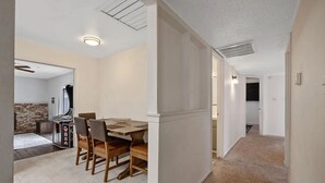 Un interior moderno con comedor que incluye una mesa y sillas de madera, cocina con salpicadero de ladrillo y pasillo con suelo alfombrado.