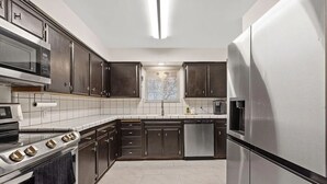 Una cocina moderna con electrodomésticos de acero inoxidable, armarios de madera oscura y un salpicadero de azulejos.