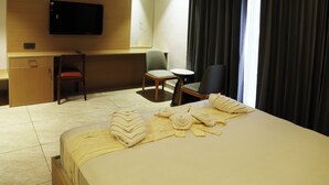 Habitación de hotel con cama, escritorio, silla, televisor y ventana con cortinas.