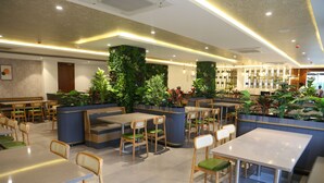 Un restaurante moderno con mesas y sillas de madera, asientos con cojines verdes y jardines verticales.