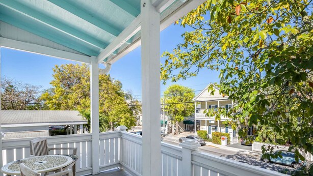 A covered porch with a table and chairs, overlooking a street with houses and cars. - Banana Split by Brightwild Pool Grill (Key West)