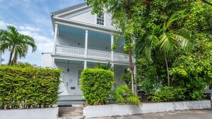 A two-story white house with a balcony, surrounded by lush greenery and palm trees. - Banana Split by Brightwild Pool Grill (Key West)