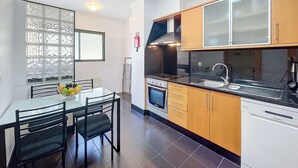 A modern kitchen with a dining table, chairs, and a fruit bowl. - Agostinho Apartment By Atlantic Holiday (Santa Cruz)