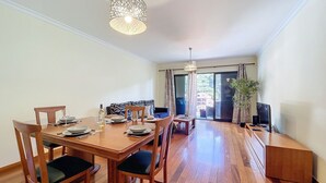 A dining area with a wooden table set for four, chairs, a hanging light fixture, and a view of the outdoors through a sliding glass door. - Agostinho Apartment By Atlantic Holiday (Santa Cruz)