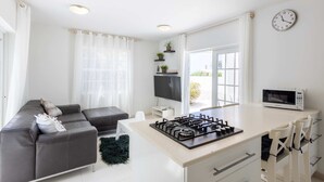A modern kitchen with a central island, a dining area with chairs, a sofa, and a flat-screen TV. - Artiko Luxury Suites - Jan Thiel (Jan Thiel)