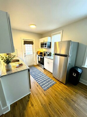 A compact kitchen with white cabinets, a stainless steel refrigerator, a microwave, and a gas stove.