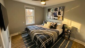 A bedroom with a bed, a ceiling fan, a window, and a wall-mounted artwork. - Modern Cozy Walk up With King Bed (Wilmington)