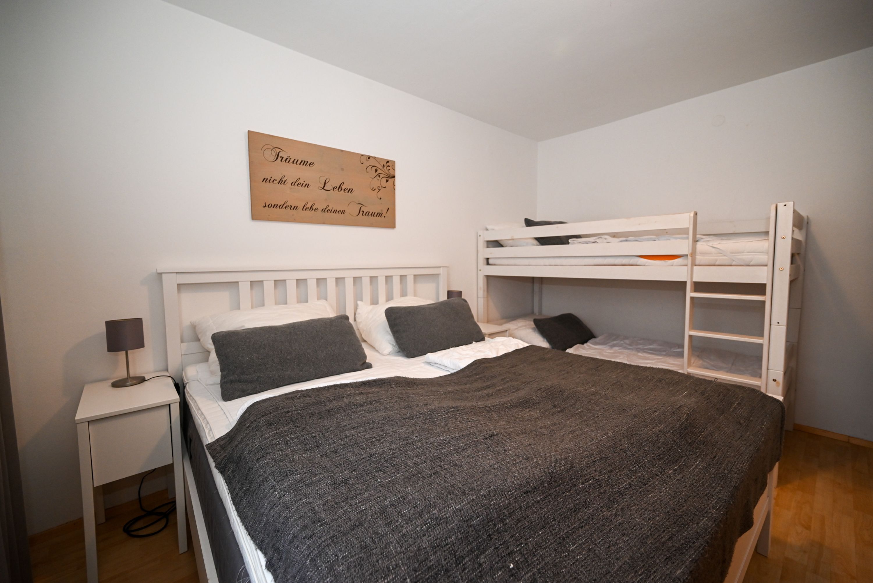 Une chambre avec un lit superposé, une table de chevet avec une lampe et un mur orné d’une citation inspirante.