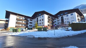 Um edifício com vários andares, varandas, área de estacionamento e neve no chão.