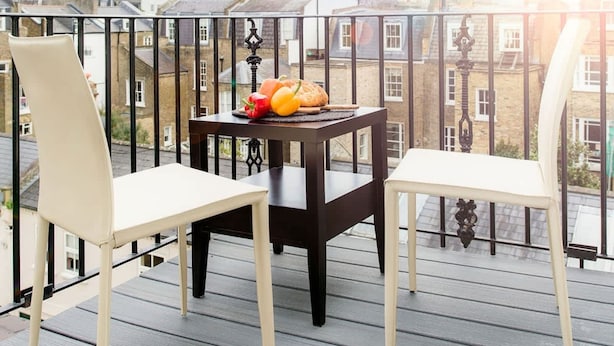 A balcony with two white chairs and a small table, a basket of fruit, and a view of buildings under a partly cloudy sky. - Bright Chelsea apt sun Terrace (London)