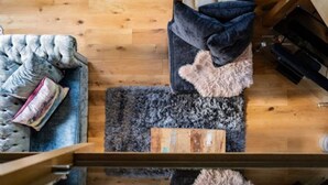A room with a wooden floor, a sofa with a fluffy rug, and a black chair with a cushion. - Host Stay The Chapel in Thornham (Hunstanton)