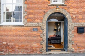 A brick building with a large arched doorway leading to a room with a bed, a lamp, and a small table. - Host Stay The Chapel in Thornham (Hunstanton)