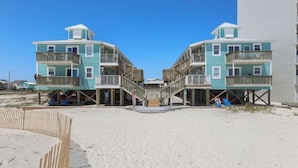 A beachfront hotel with two-story buildings, wooden balconies, and a sandy beach in the foreground. - Sunrise Village 215- 2BR 1BA Gulf Front Sleep 6 (Gulf Shores)