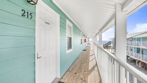 A covered wooden corridor with a white door marked '215', a wooden floor, and a railing overlooking a balcony area. - Sunrise Village 215- 2BR 1BA Gulf Front Sleep 6 (Gulf Shores)