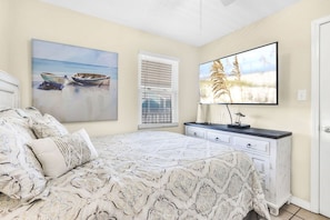 Une chambre à coucher comprenant un lit, une commode, un téléviseur et deux tableaux accrochés au mur.