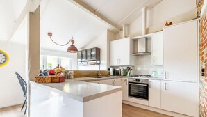 A modern kitchen with white cabinetry, a central island, and a hanging pendant light. - Host Stay Nicholson Cottage (North Walsham)