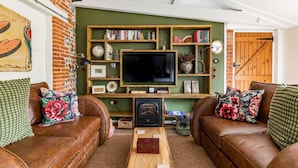A cozy living room with a fireplace, leather sofas, a wooden bookshelf, and a television. - Host Stay Nicholson Cottage (North Walsham)