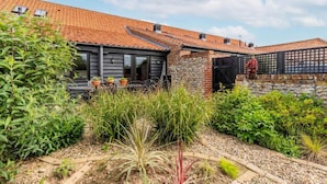 A house with a tiled roof, a stone wall, and a garden with various plants. - Host Stay Nicholson Cottage (North Walsham)