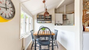 A dining area with a wooden table and black chairs, a hanging light fixture, and a clock on the wall. - Host Stay Nicholson Cottage (North Walsham)