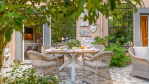 An outdoor dining area with wicker furniture, a table set for four, surrounded by greenery and a stone floor. - The Garden Lodge in Lucca (Lucca)