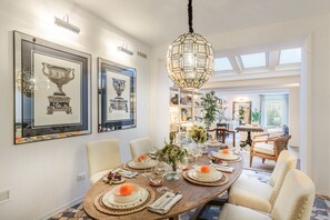A dining area with a long table set for a meal, framed artwork on the walls, and a chandelier. - The Garden Lodge in Lucca (Lucca)