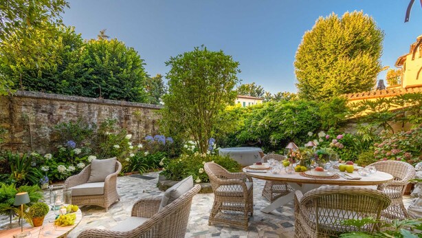A patio with wicker furniture, a stone floor, and lush greenery. - The Garden Lodge in Lucca (Lucca)
