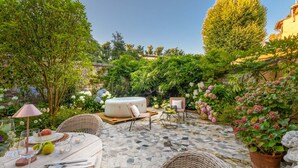 An outdoor patio with a hot tub, wicker furniture, and a stone-tiled floor. - The Garden Lodge in Lucca (Lucca)