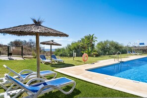 Piscina com espreguiçadeiras e guarda-sóis, cercada por vegetação e um céu azul.