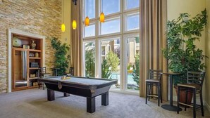 A pool table in a room with large windows, a bookshelf, and potted plants. - New Upscale 1BR Stay With Mini Golf Sauna Heated Pool (Reno)
