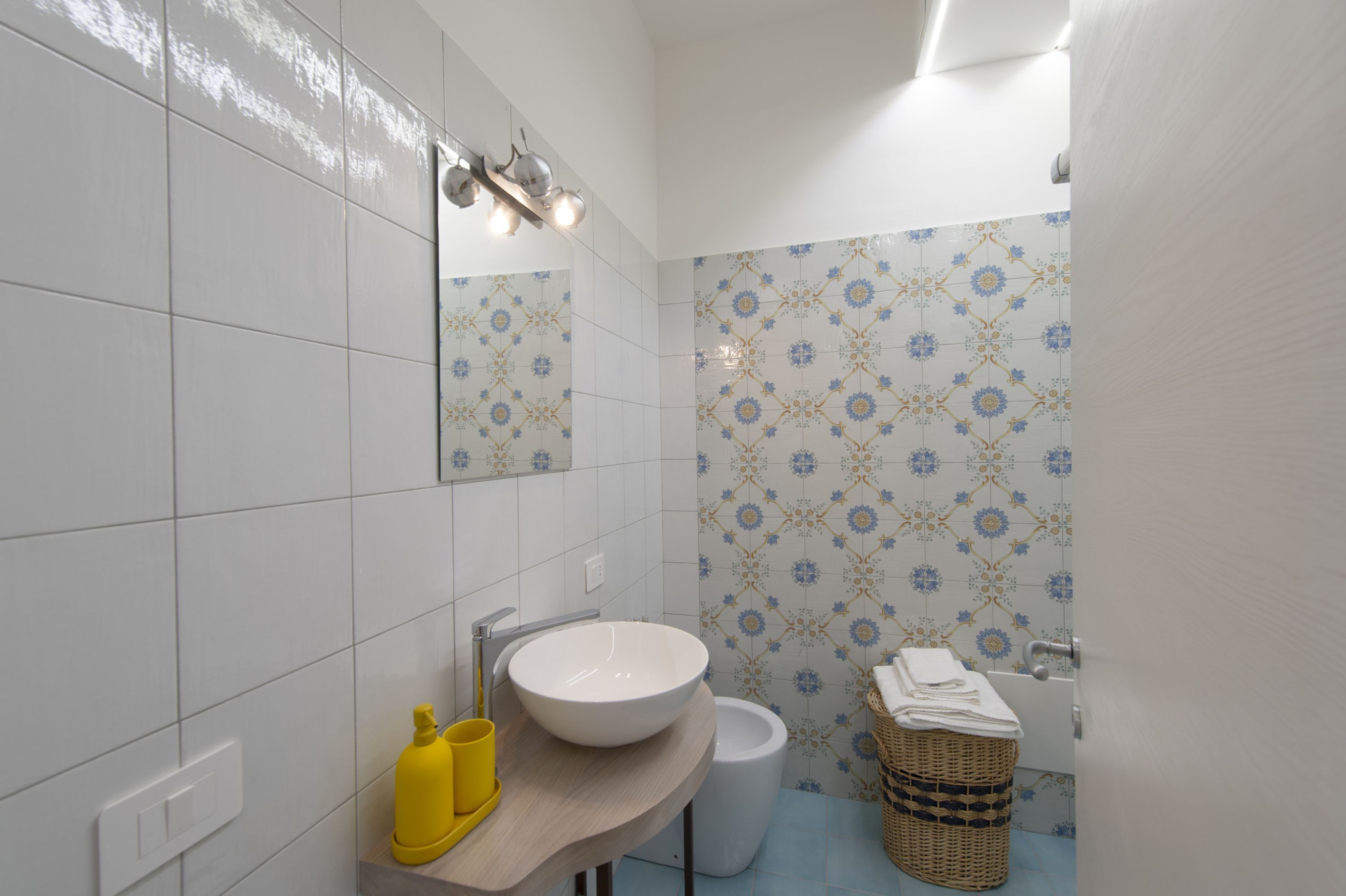 A bathroom with a white sink, a mirror, a yellow soap dispenser, a white toilet, and a patterned wall.