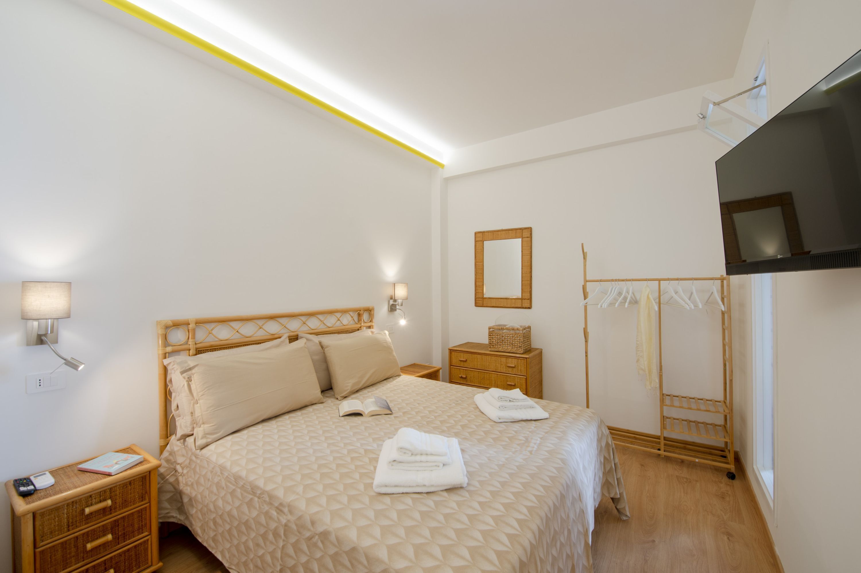 A neatly arranged bedroom with a bed, bedside tables, a mirror, and a drying rack.